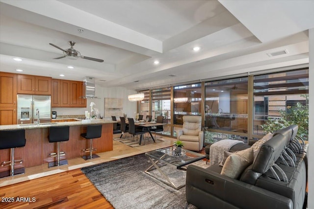 living area featuring light wood-style floors, visible vents, a tray ceiling, and recessed lighting