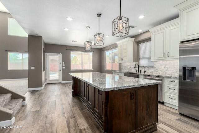 1051 E Julie Ave, San Tan Valley, AZ 85140 - kitchen featuring light wood-style floors, dark brown cabinets, a kitchen island, stainless steel appliances, and backsplash