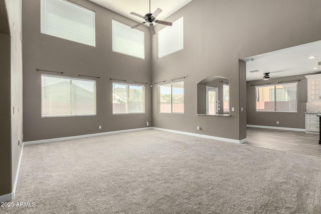1051 E Julie Ave, San Tan Valley, AZ 85140 - unfurnished living room with baseboards, arched walkways, ceiling fan, carpet, and a towering ceiling