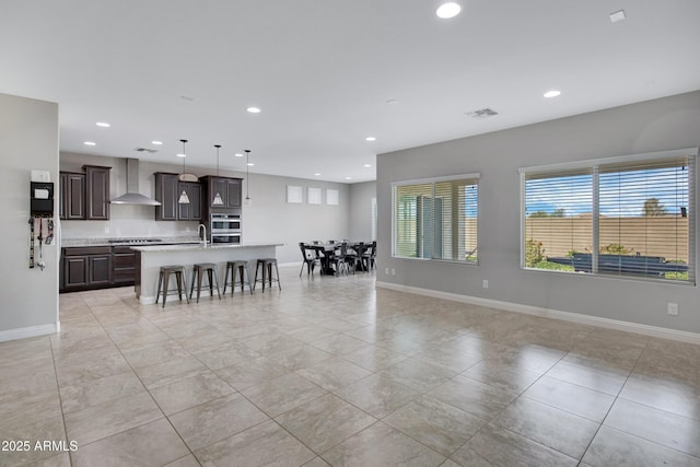 kitchen with cooktop, visible vents, light countertops, wall chimney range hood, and a kitchen bar