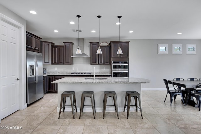 kitchen with dark brown cabinetry, visible vents, wall chimney exhaust hood, stainless steel appliances, and a sink