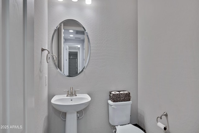 bathroom featuring toilet, visible vents, and a textured wall
