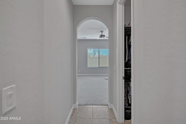 corridor with arched walkways, light colored carpet, baseboards, and light tile patterned floors