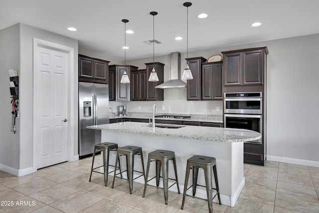 kitchen featuring stainless steel appliances, a sink, visible vents, dark brown cabinets, and wall chimney range hood