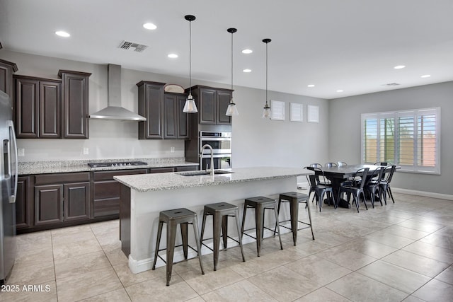 kitchen featuring visible vents, wall chimney exhaust hood, appliances with stainless steel finishes, a breakfast bar area, and a sink