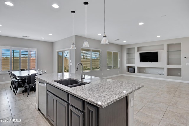 kitchen with built in shelves, a kitchen island with sink, a sink, baseboards, and stainless steel dishwasher
