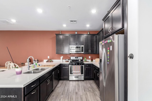 kitchen with light wood-type flooring, kitchen peninsula, sink, and appliances with stainless steel finishes