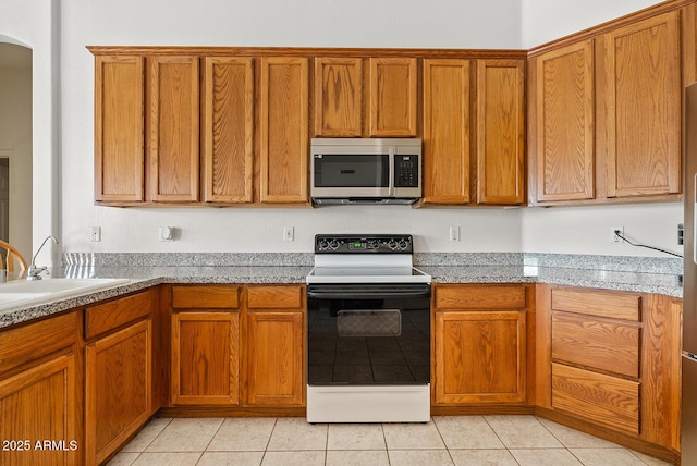 4701 W Fallen Leaf Ln, Glendale, AZ 85310 - kitchen with stainless steel microwave, range with electric cooktop, brown cabinetry, and light tile patterned floors