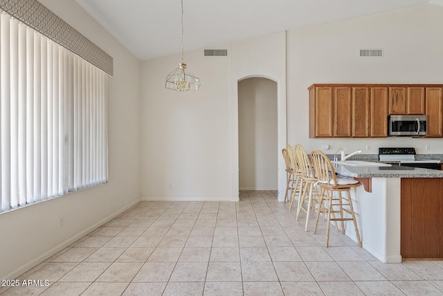 4701 W Fallen Leaf Ln, Glendale, AZ 85310 - kitchen with range with electric stovetop, stainless steel microwave, arched walkways, brown cabinets, and light stone counters