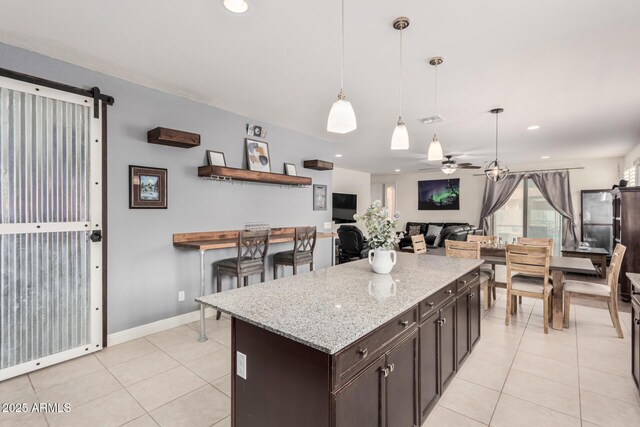 kitchen featuring dark brown cabinetry, light tile patterned floors, ceiling fan, light stone countertops, and pendant lighting