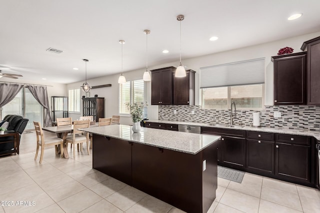 kitchen featuring dark brown cabinetry, a kitchen island, a sink, backsplash, and light stone countertops