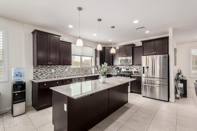 kitchen featuring light stone countertops, dark brown cabinetry, appliances with stainless steel finishes, and a center island