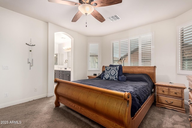 carpeted bedroom featuring arched walkways, visible vents, ensuite bathroom, ceiling fan, and baseboards