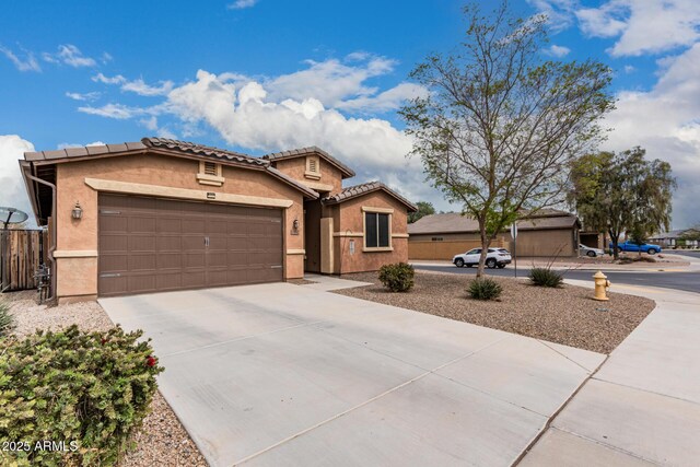 view of front of property featuring concrete driveway, a tiled roof, an attached garage, fence, and stucco siding