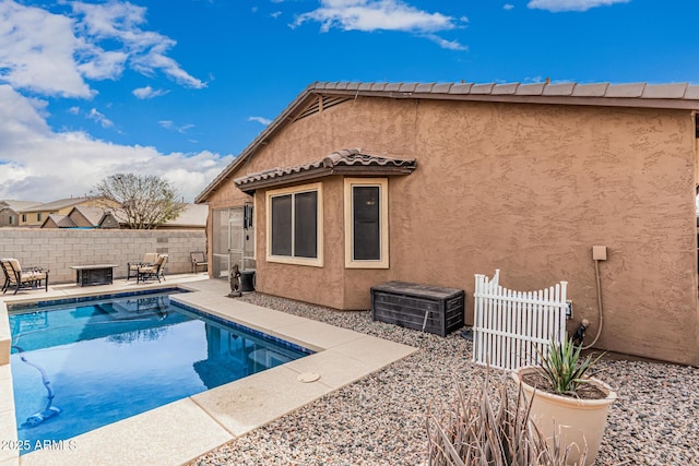 back of property featuring a tiled roof, fence, a fenced in pool, and stucco siding