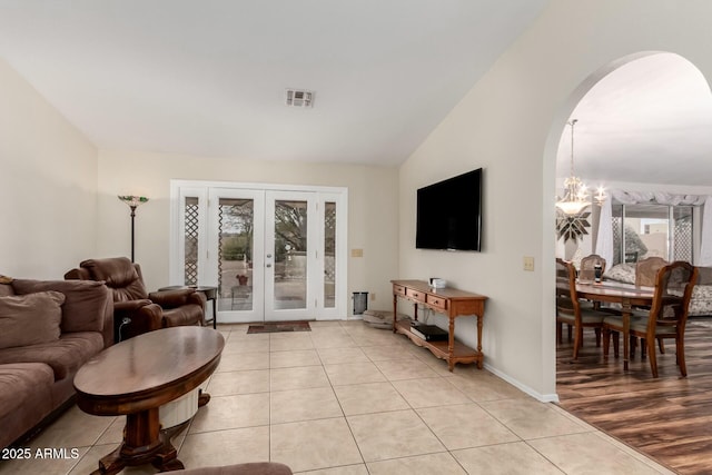 tiled living room featuring lofted ceiling, an inviting chandelier, and french doors