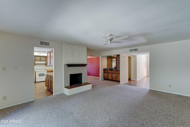 unfurnished living room featuring light carpet, a large fireplace, and ceiling fan