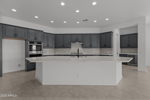 21541 W Mariposa St, Buckeye, AZ 85396 - kitchen with wine cooler, a large island, backsplash, light stone counters, and under cabinet range hood