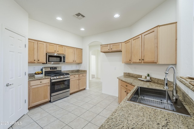 kitchen featuring arched walkways, visible vents, appliances with stainless steel finishes, light brown cabinets, and a sink