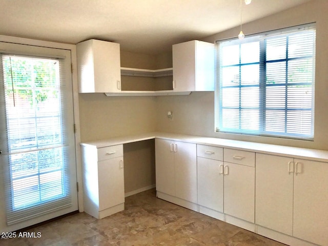 kitchen with white cabinets, pendant lighting, built in desk, and a wealth of natural light