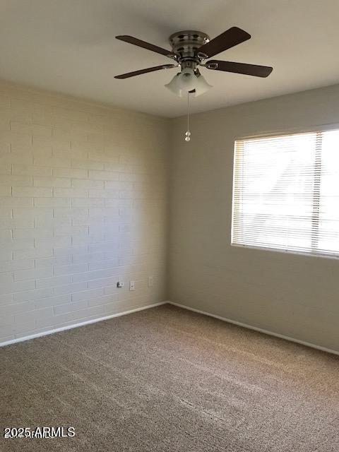 carpeted empty room featuring ceiling fan and brick wall