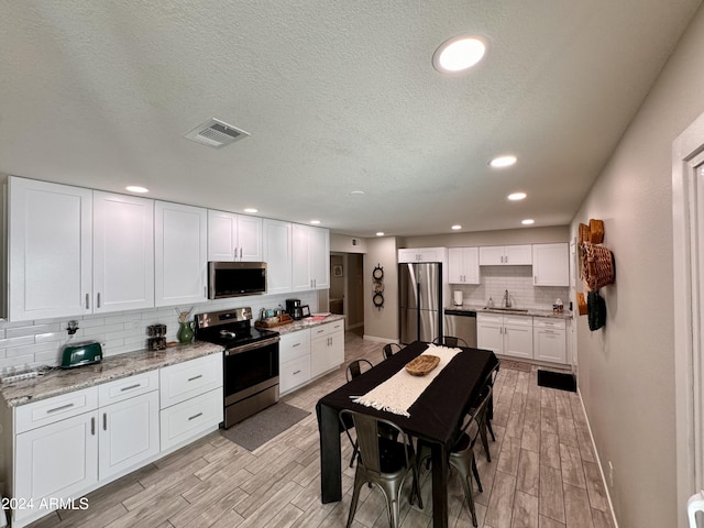 kitchen with decorative backsplash, white cabinets, light hardwood / wood-style flooring, sink, and stainless steel appliances