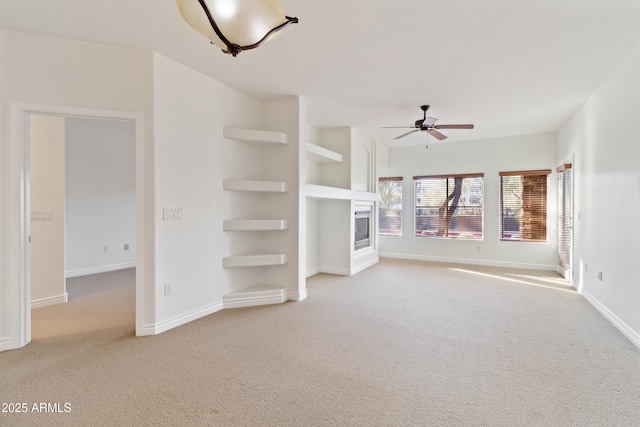 unfurnished living room with built in shelves, light colored carpet, and ceiling fan