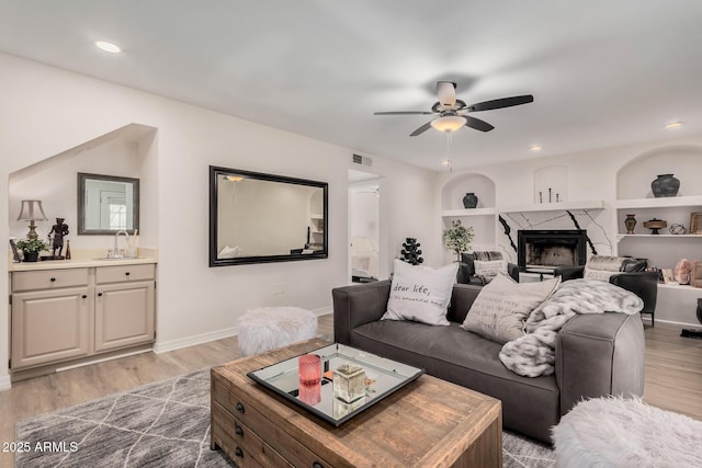 living room with sink, light hardwood / wood-style flooring, built in features, ceiling fan, and a fireplace