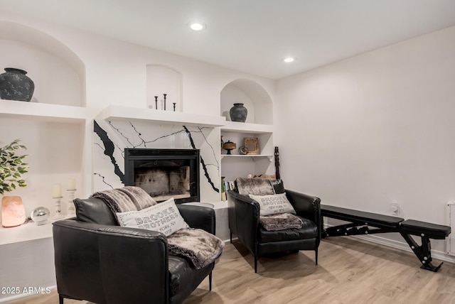 living area with a premium fireplace, built in features, and light wood-type flooring