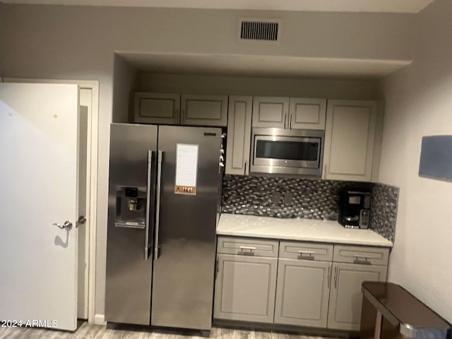 kitchen with backsplash, stainless steel appliances, gray cabinets, and light hardwood / wood-style flooring