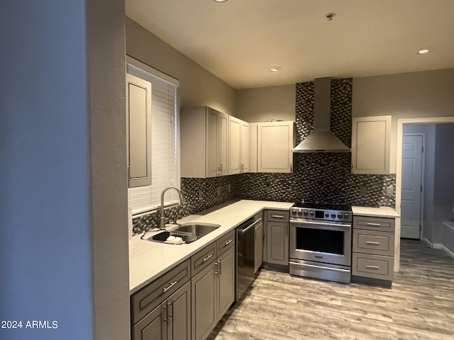 kitchen with gray cabinetry, wall chimney exhaust hood, sink, and stainless steel appliances