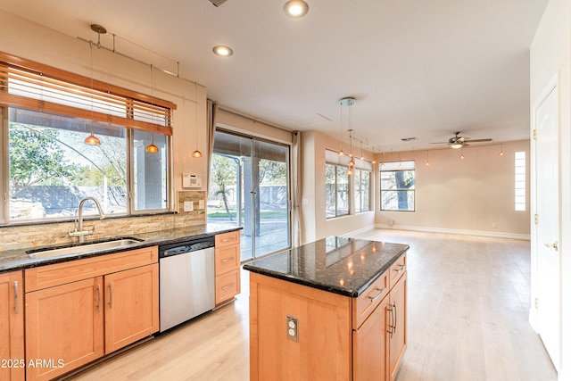 kitchen featuring a kitchen island, a sink, hanging light fixtures, stainless steel dishwasher, and dark stone counters