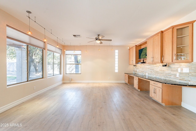 kitchen with visible vents, hanging light fixtures, light brown cabinetry, glass insert cabinets, and dark stone counters