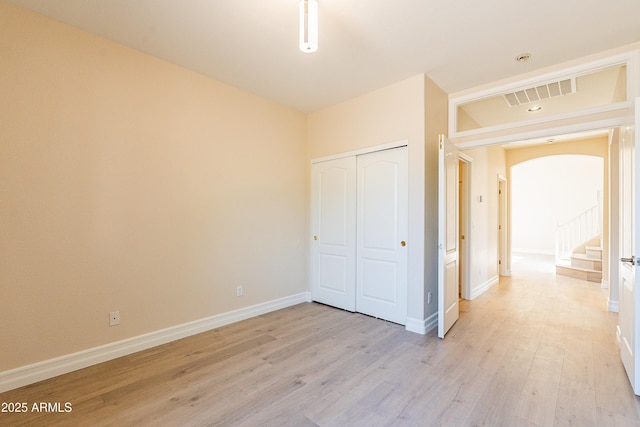 unfurnished bedroom with arched walkways, a closet, visible vents, light wood-type flooring, and baseboards