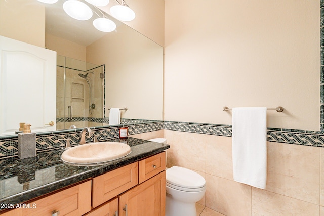 full bathroom with a wainscoted wall, tile walls, toilet, vanity, and tiled shower