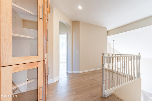 corridor with baseboards, arched walkways, wood finished floors, an upstairs landing, and recessed lighting