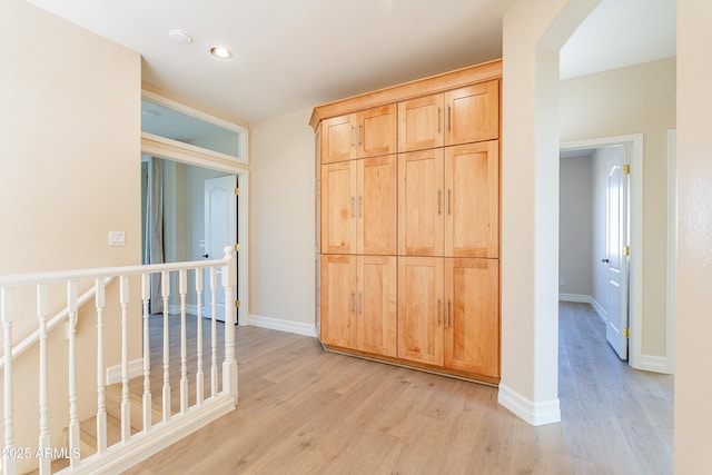 hallway featuring light wood-type flooring, arched walkways, and baseboards