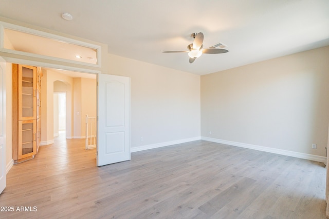 unfurnished room with light wood-type flooring, ceiling fan, arched walkways, and baseboards