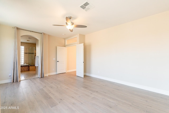 unfurnished bedroom featuring arched walkways, baseboards, visible vents, and light wood finished floors