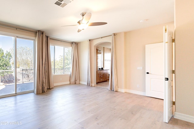 unfurnished room featuring arched walkways, visible vents, baseboards, a ceiling fan, and light wood-type flooring