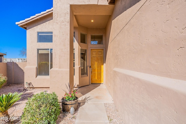 view of exterior entry with a tile roof, fence, and stucco siding