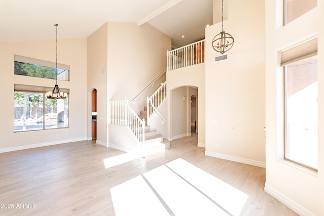 unfurnished living room featuring a chandelier, arched walkways, light wood-type flooring, and stairs