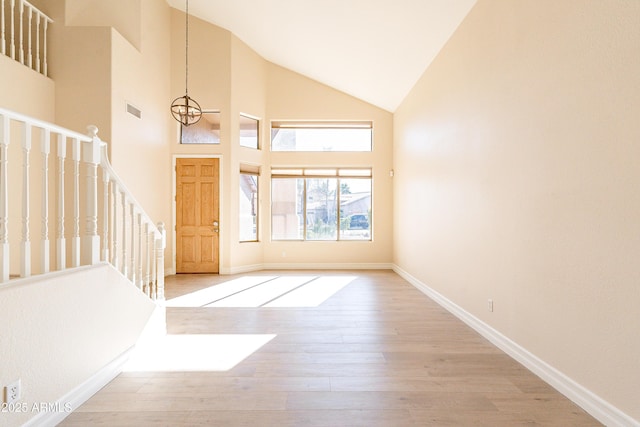 entryway with visible vents, high vaulted ceiling, light wood-type flooring, baseboards, and stairs