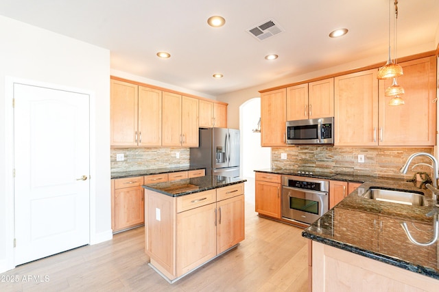 kitchen with light brown cabinets, a sink, hanging light fixtures, appliances with stainless steel finishes, and dark stone countertops