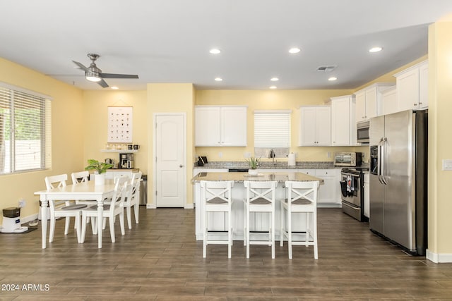 kitchen featuring dark hardwood / wood-style flooring, a breakfast bar, stainless steel appliances, a center island, and white cabinetry