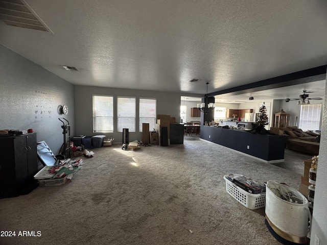 unfurnished living room featuring ceiling fan with notable chandelier, carpet, and a textured ceiling