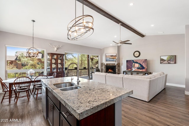 kitchen featuring decorative light fixtures, lofted ceiling with beams, a lit fireplace, and a sink