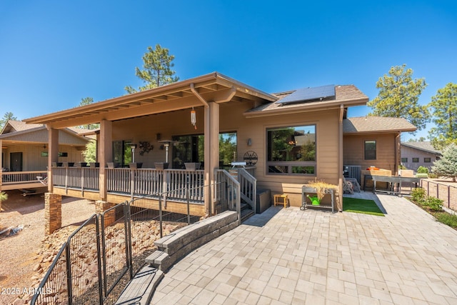 rear view of house featuring a patio, fence, a shingled roof, and roof mounted solar panels