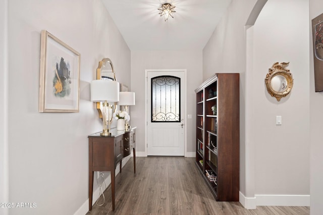 entrance foyer featuring wood finished floors, arched walkways, and baseboards