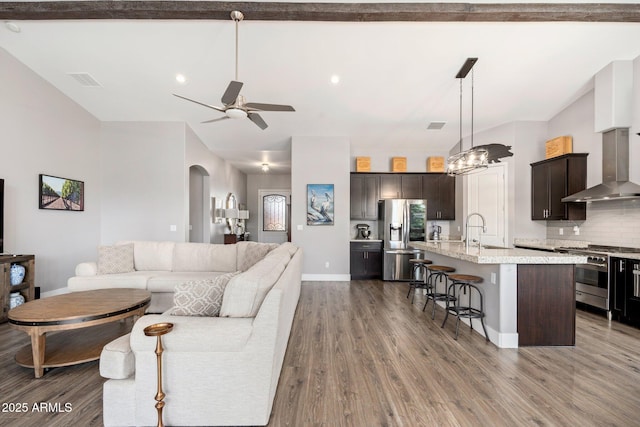 living area with wood finished floors, a ceiling fan, visible vents, and arched walkways